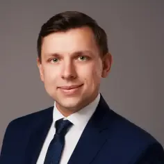 Portret mężczyzny w granatowym garniturze i krawacie na szarym tle.