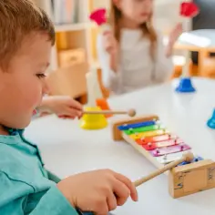 Chłopiec aktywnie w żłobku gra na cymbałkach, obok inne dzieci dzwonią dzwonkami.