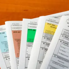 Stosy formularzy podatkowych PIT-38, PIT-37, PIT-36, PIT-36L i PIT-28 leżą na drewnianym blacie.