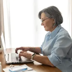 Kobieta w okularach pracuje na laptopie. To jej okres ochronny przed emeryturą, więc jeszcze aktywnie działa zawodowo.
