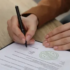 Dłoń podpisuje dokument, na którym widnieje pieczęć "LICENSED". To ważny krok do uzyskania licencji.