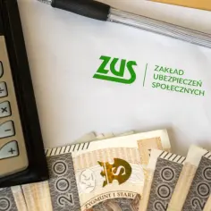Kalkulator, długopis, dokument ZUS i polskie banknoty. Obrazek sugeruje rozliczenia związane z chorobowym.