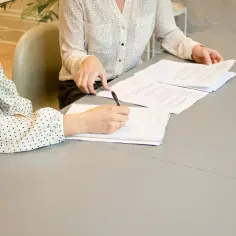 Dwie kobiety przy stole analizują dokumenty. Jedna pisze, druga przegląda akta. Gdzie numer aktu notarialnego?