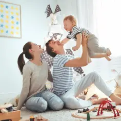 Szczęśliwa rodzina cieszy się wspólnym czasem. Ojciec podrzuca dziecko, mama patrzy z uśmiechem. To idealny urlop rodzicielski 9 tygodni.