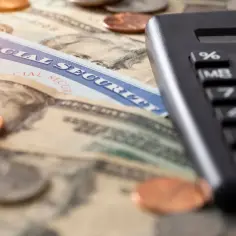 Karta Social Security, banknoty i monety leżą obok kalkulatora, sugerując obliczenia dotyczące danych płatnika składek.