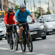 Dwóch rowerzystów w kaskach jedzie po ulicy, mijając samochody. Czy można jeździć rowerem po chodniku? Tutaj widać, że nie.