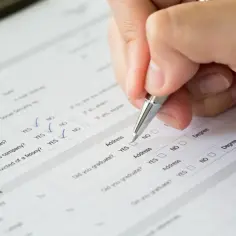 Ręka z długopisem wypełnia formularz, zaznaczając odpowiedzi. Czy do PCC trzeba dołączyć umowę? Formularz zawiera pytania o obywatelstwo i wykształcenie.