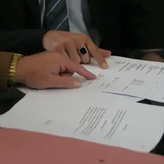 Dłonie wskazujące na dokumenty z tabelami i tekstem.