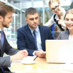 Zespół przy biurku analizuje dane. Młody pracownik młodociany uczy się od starszych kolegów.