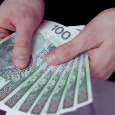 Dłonie trzymają stos banknotów 100 zł. Czy to już wynagrodzenie minimalne 2026?