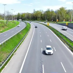 Autostrada z zielonymi pasami i drzewami. Samochody jadą z różną prędkością, ale żadne nie przekracza minimalnej prędkości na autostradzie.