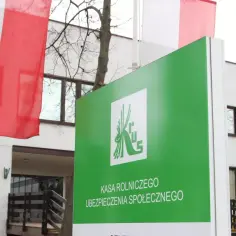 Zielony znak Kasy Rolniczego Ubezpieczenia Społecznego, gdzie można uzyskać ubezpieczenie chorobowe. W tle polskie flagi.
