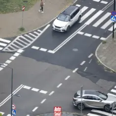 Na skrzyżowaniu równorzędnym dwa samochody zbliżają się do pasów. Jeden biały, drugi srebrny.