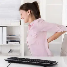 Kobieta w biurze odczuwa ból pleców, objaw choroby zawodowej.