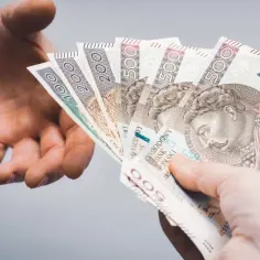 Przekazanie gotówki, symbolizujące jak wypłacić pieniądze z PPK. Dłonie przekazują sobie polskie banknoty o nominałach 100, 200 i 500 zł.