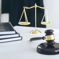 Młotek sędziowski, waga sprawiedliwości i stos książek na białym biurku.