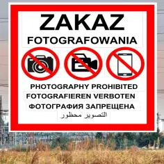Znak ZAKAZ FOTOGRAFOWANIA na tle linii energetycznych i stacji transformatorowej.