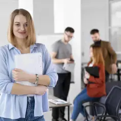 Uśmiechnięta kobieta z notatnikiem, w tle zespół dyskutujący o możliwościach, jakie daje dofinansowanie z urzędu pracy.