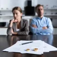 Para rozwiedzionych siedzi przy stole, na którym leżą dokumenty rozwodowe i obrączki.