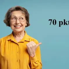 Uśmiechnięta starsza pani w żółtej bluzce wskazuje kciukiem na napis "70 pkt", sugerując świadczenie wspierające punkty.
