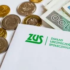 ZUS i pieniądze, które czekają na każdego emeryta. Monety i banknoty leżą obok dokumentu z logo ZUS.