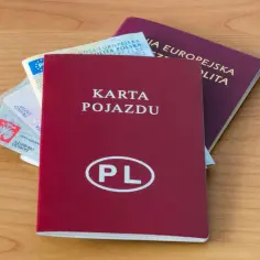 Czerwona rejestracja, dowód osobisty, prawo jazdy i paszport leżą na drewnianym blacie.