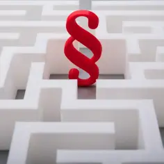 Czerwony symbol paragrafu, symbolizujący akt prawny o charakterze ogólnym, znajduje się w centrum białego labiryntu.