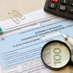 Formularz PIT-38 jak wypełnić? Dokument, kalkulator, długopis i lupa na banknocie 100 zł wskazują na rozliczenie dochodów.