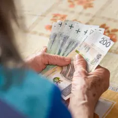 Dłonie starszej osoby liczą banknoty 200 zł. Może to być pomocne przy analizie 14 emerytura tabela netto.
