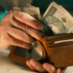Dłonie wkładają polskie banknoty do brązowego portfela. Czy to wystarczy na minimalną stawkę godzinową netto?