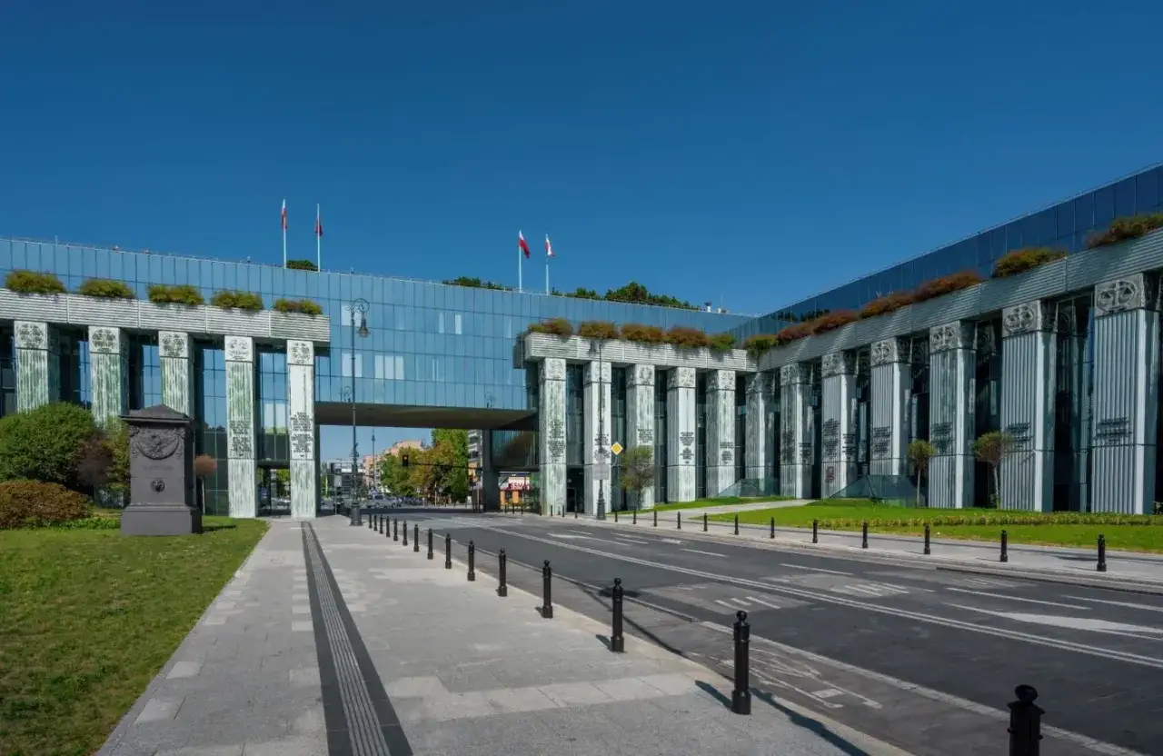 Nowoczesny budynek Sądu Najwyższego, gdzie mieści się Izba Kontroli Nadzwyczajnej i Spraw Publicznych, z charakterystycznymi kolumnami i szklaną fasadą.