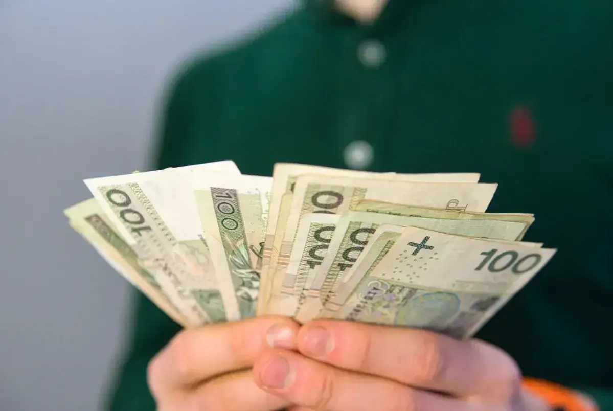 Dłonie trzymają wachlarz banknotów 100 zł. Może to być wypłata, oszczędności lub emerytura.