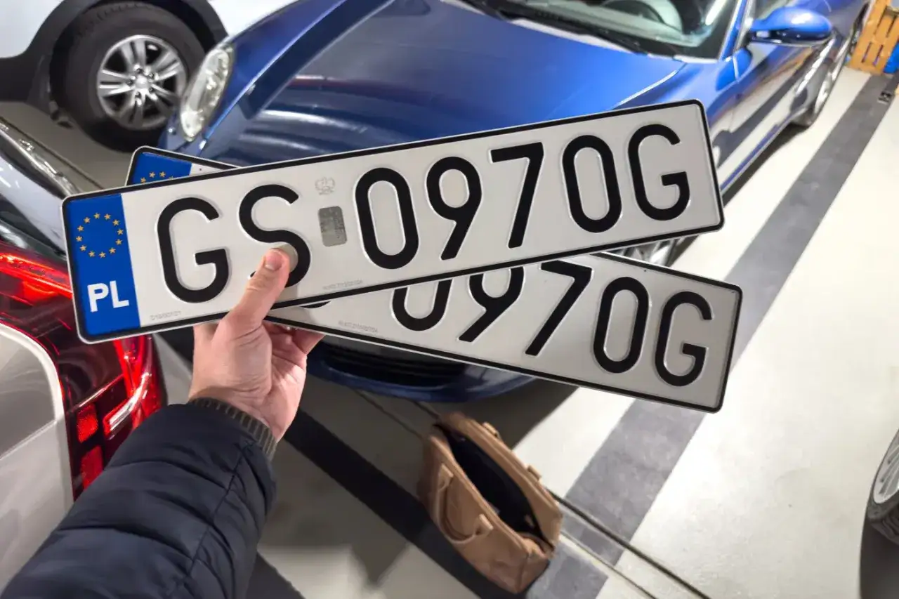 Ręka trzyma tablice rejestracyjne GS 0970G. Unikaj kary za nieprzerejestrowanie samochodu, wymień tablice!