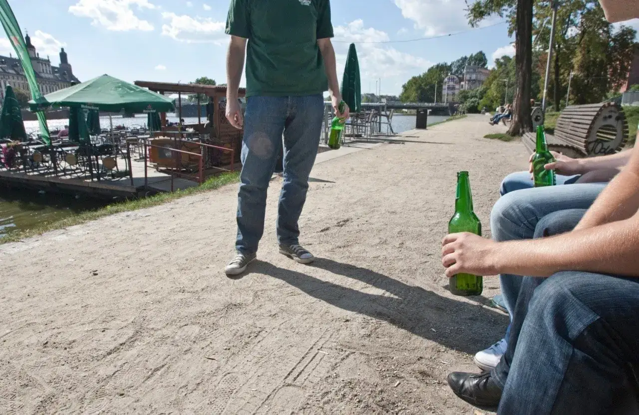 Ludzie piją piwo nad rzeką, narażając się na mandat za picie w miejscu publicznym.