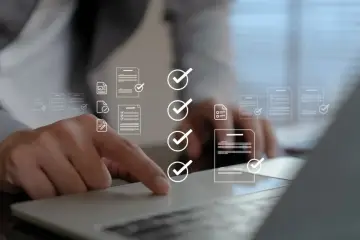 Dłoń na touchpadzie laptopa, nad nią wirtualne dokumenty z zaznaczonymi zadaniami. Proces weryfikacji i zatwierdzania dokumentów, jak np. NIP-2.