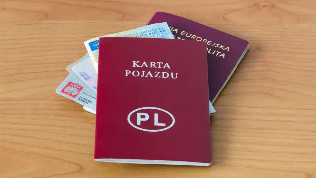 Czerwona rejestracja, dowód osobisty, prawo jazdy i paszport leżą na drewnianym blacie.